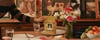 Hand placing a Golden Child fresh dog food pouch on a dinner table set with flowers and fruit
