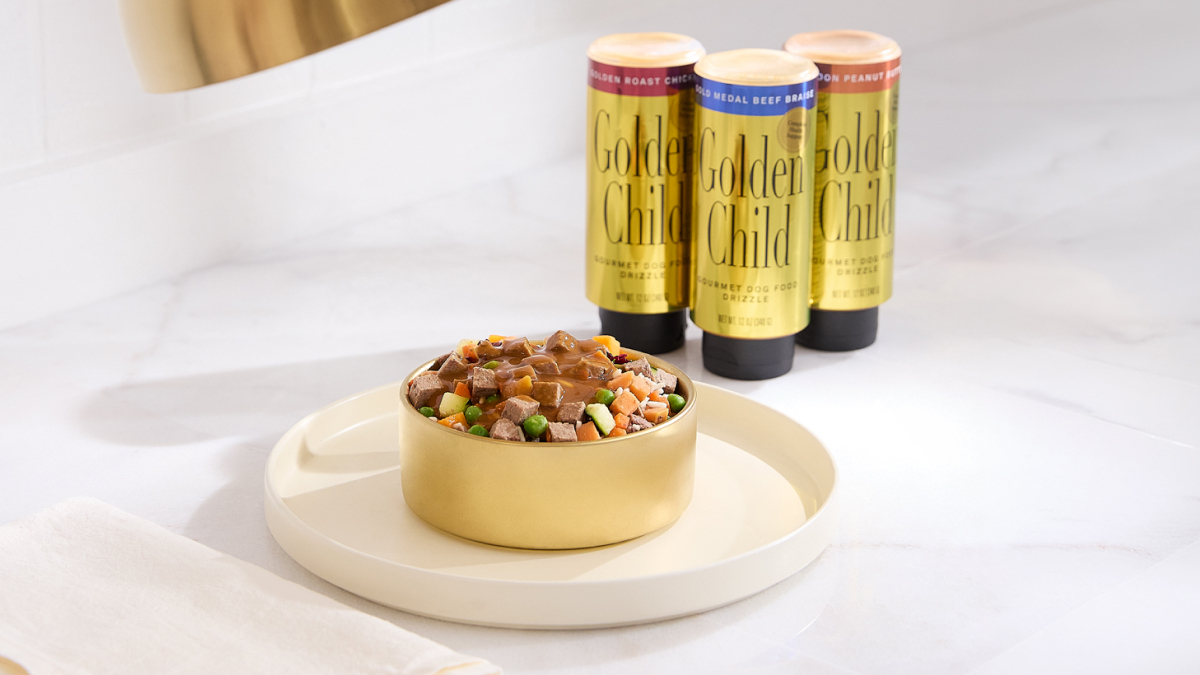 Bowl of fresh dog food topped with gravy beside three Golden Child drizzle dog food toppers