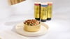 Bowl of fresh dog food topped with gravy beside three Golden Child drizzle dog food toppers